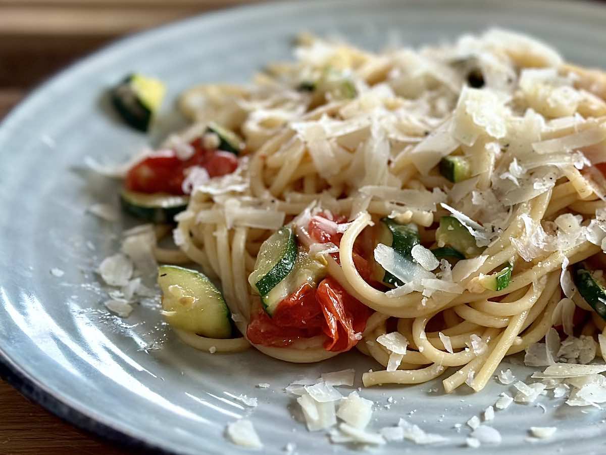 Makaron z cukinią i pomidorkami koktajlowymi, posypany tartym parmezanem, podany na talerzu