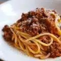 Spaghetti bolognese posypane tartym parmezanem, podane na talerzu