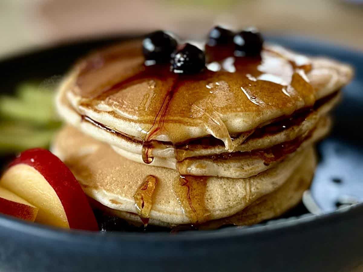 Pancakes podane z syropem klonowym, porzeczkami i nektarynką na talerzu