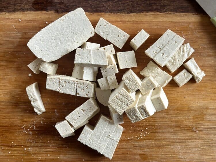 Tofu pokrojone na małe kawałki na drewnianej desce