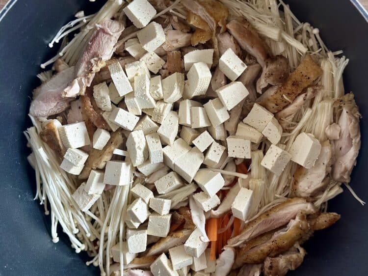 Kurczak, tofu, marchewka i grzyby ułożone w garnku przed dodaniem bulionu